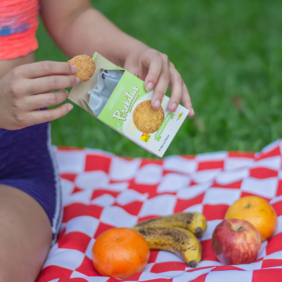 Unas manos sacan una galleta de su caja en un picnic con fruta sobre mantel de cuadros
