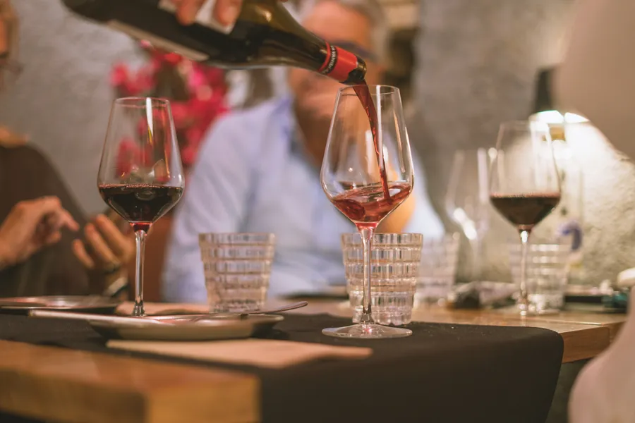 Un camarero sirve vino tinto en las copas de una mesa