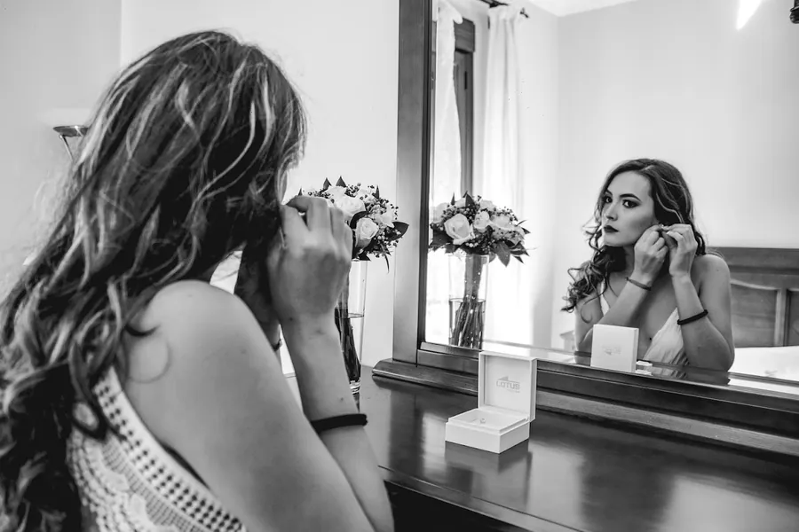 Retrato en blanco y negro de una novia arreglándose frente al espejo