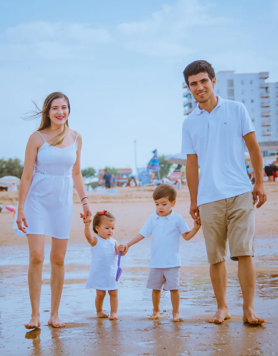Una familia con dos niños pequeños camina descalza por la orilla de la playa