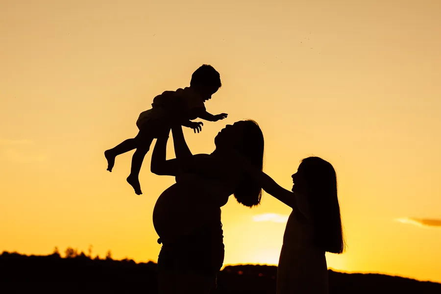 Silueta de una madre levantando a su bebé al atardecer junto a su hija