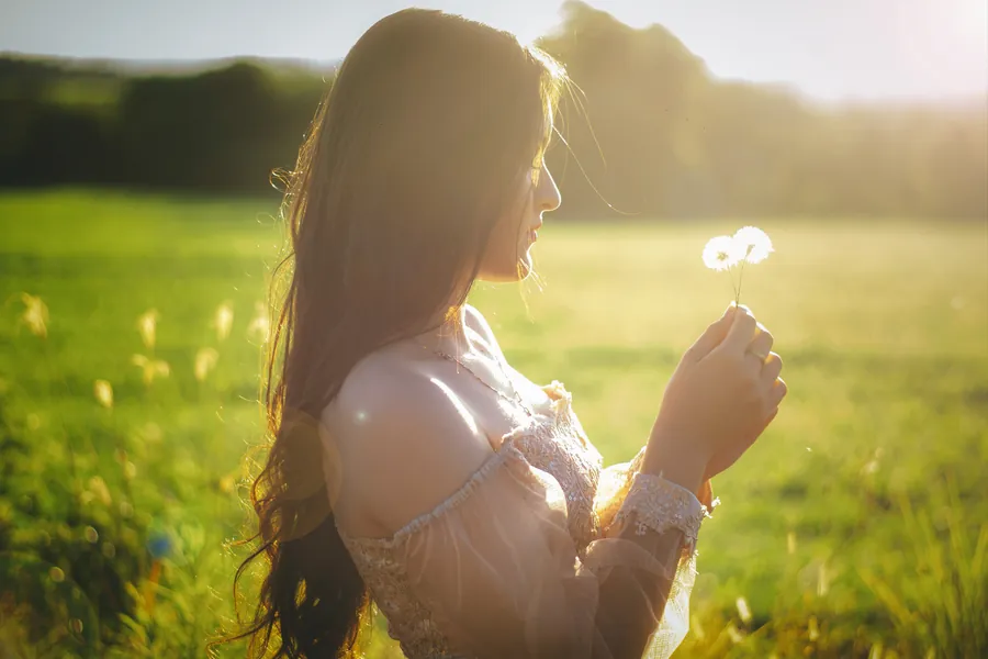 Retrato de una mujer con una flor en la mano en un campo al atardecer