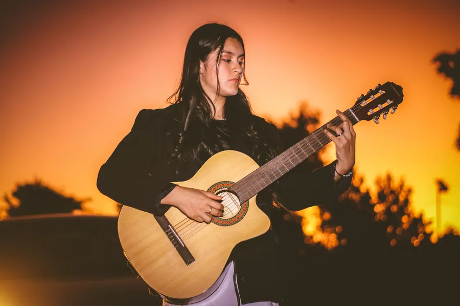 Una joven toca la guitarra frente a un cielo naranja al atardecer