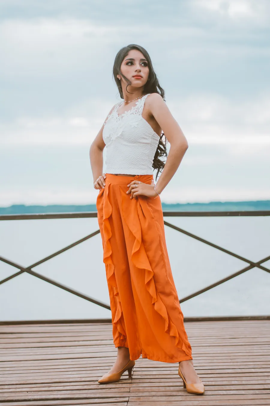 Una joven con pantalón naranja posa en un muelle junto al río