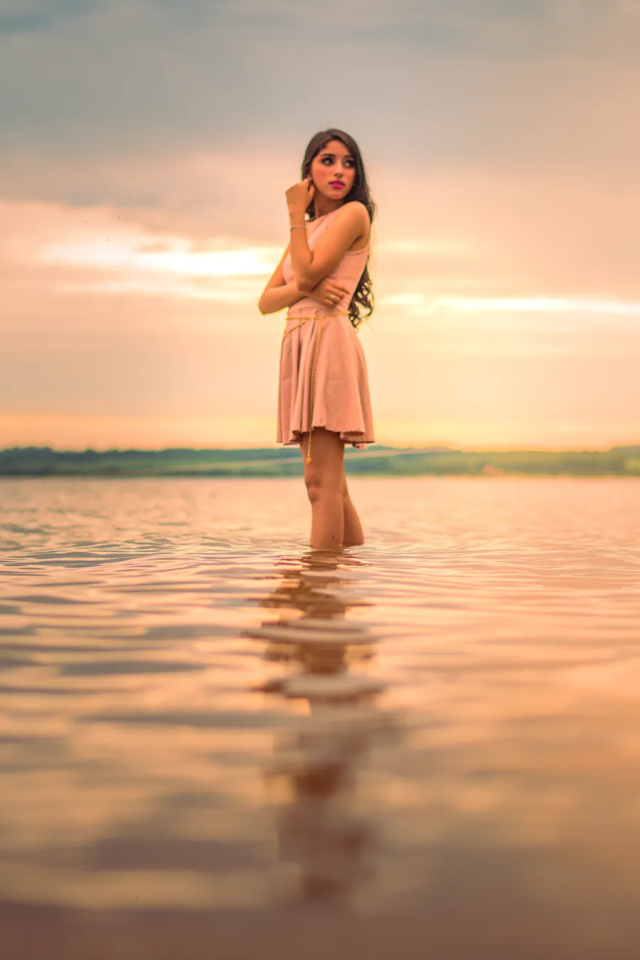 Una joven con vestido rosa de pie en el agua con el cielo del atardecer reflejado